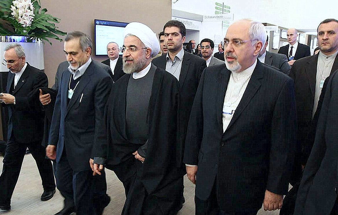 این تصویر گروهی از افراد را نشان می‌دهد که در حال حرکت به سمت یک مکان هستند. یکی از آنها به وضوح لباس روحانیت پوشیده و دیگران نیز به طور رسمی لباس پوشیده‌اند. به نظر می‌رسد این افراد در یک رویداد یا کنفرانس رسمی شرکت کرده‌اند. محیط تصویر ممکن است یک مکان اداری یا کنفرانس باشد که نشان‌دهنده تعاملات سیاسی یا اقتصادی است.