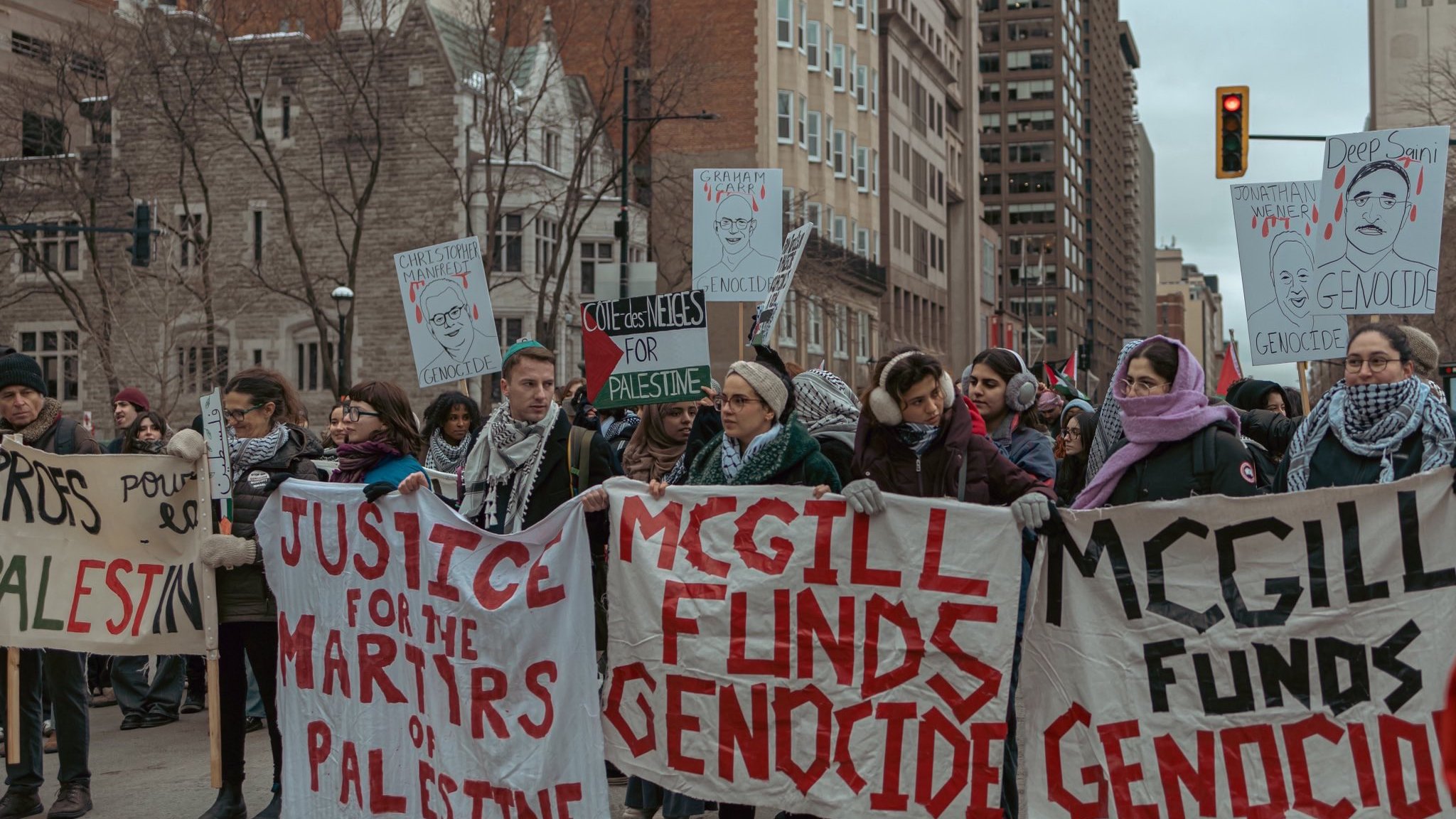 The image depicts a group of protesters marching in a city setting. They are holding banners and signs with messages emphasizing justice for Palestine and accusing McGill University of funding genocide. The atmosphere appears serious and focused, with the protesters displaying solidarity on the issue. The urban environment features tall buildings in the background, indicating that this is a public demonstration.