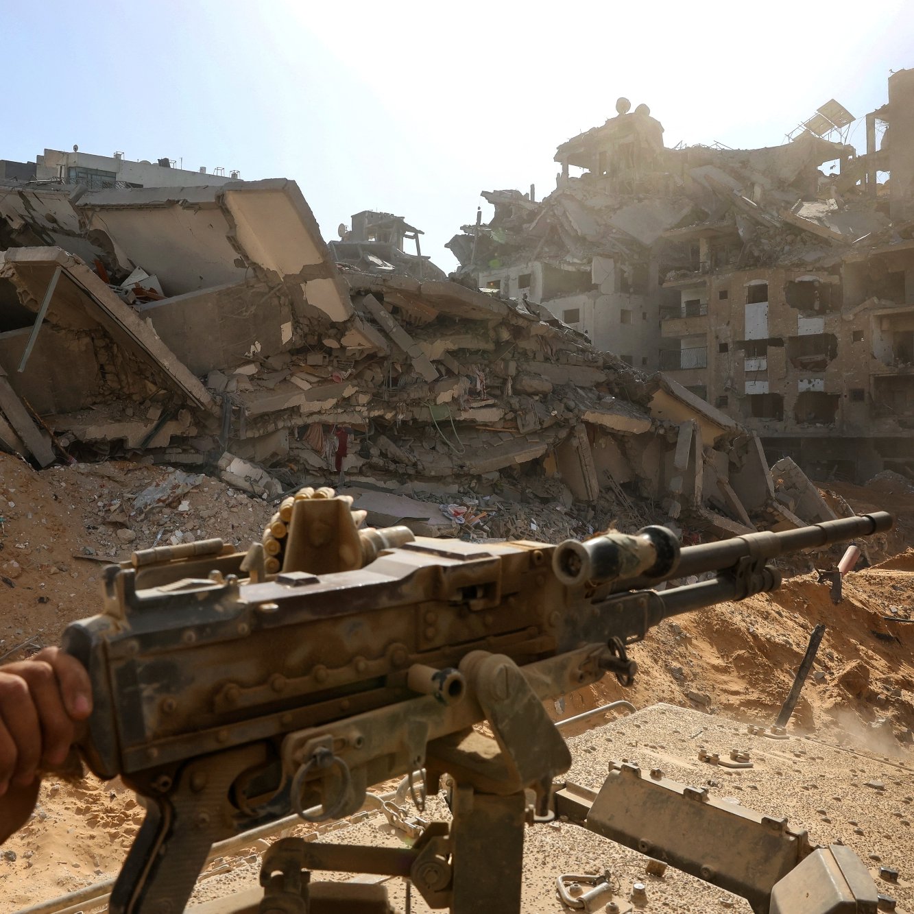 تصویری از یک منطقه ویران‌شده، با ساختمان‌های خراب و تفنگی در پیش‌زمینه. غبار و تابش نور خورشید در آسمان.