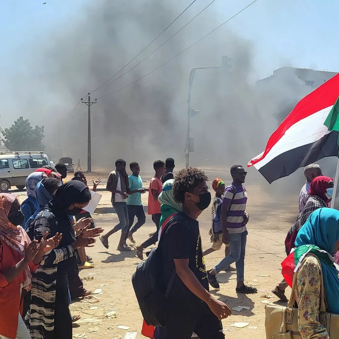 Manifestanti con bandiera del Sudan, in mezzo a fumi di incendi e tensione.