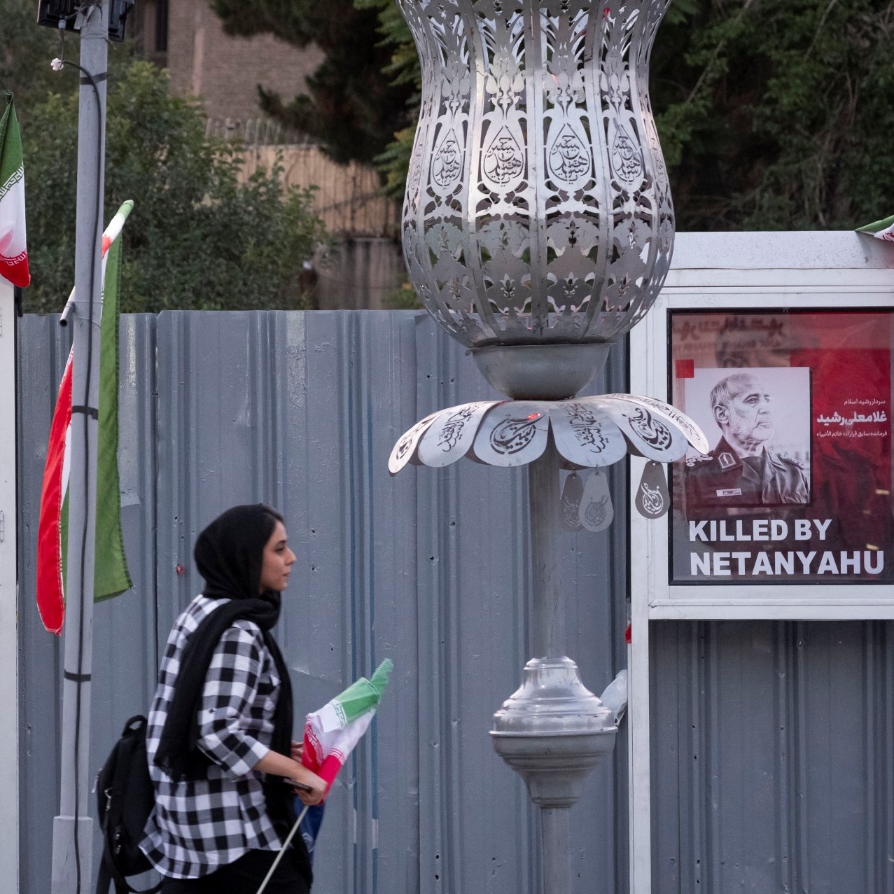 A woman walks past two posters stating "Killed by Netanyahu," with flags nearby.