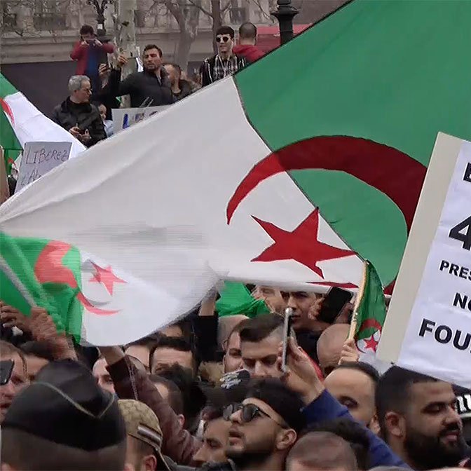 الصورة تظهر مجموعة من المحتجين في تظاهرة، يحملون أعلام الجزائر بالإضافة إلى لافتة مكتوب عليها "ERROR 404 PRESIDENT NOT FOUND". تعكس هذه الصورة مشاعر الاحتجاج والمطالبة بالتغيير السياسي، حيث يُظهر المتظاهرون تصميمهم على المطالبة بحقوقهم وبإصلاحات في البلاد. الأجواء تبدو حماسية ومليئة بالروح الوطنية.