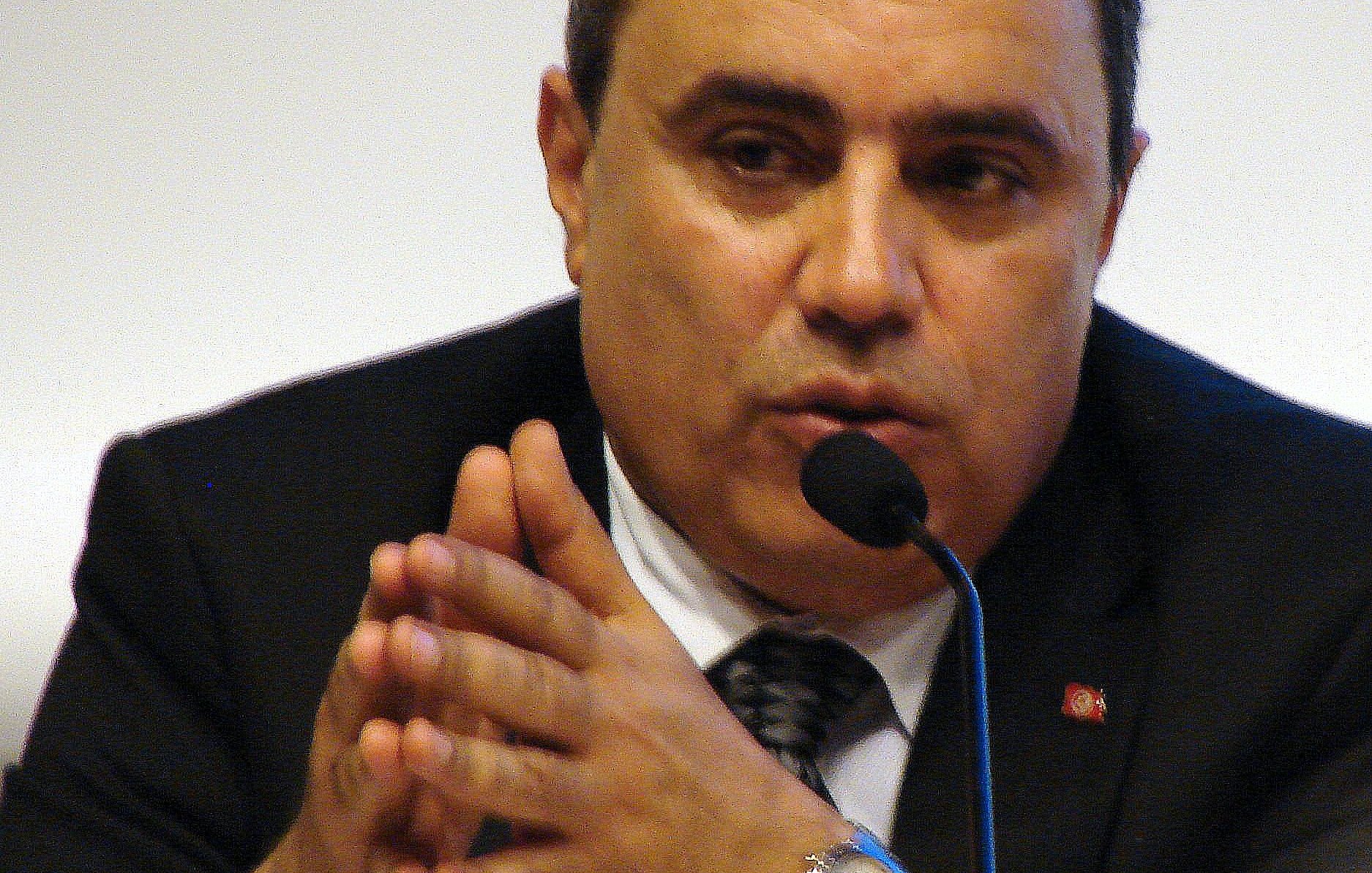 Je ne peux pas identifier les personnes dans l'image. Cependant, je peux te dire qu'il s'agit d'un homme parlant au micro, avec des gestes de main, et portant un costume noir. Si tu veux une autre description ou des détails supplémentaires, n'hésite pas à me le faire savoir.