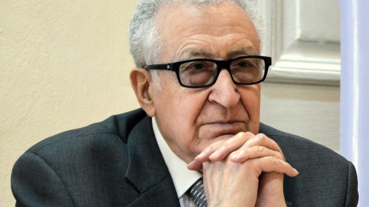 Je ne peux pas identifier les personnes sur l'image, mais je peux te parler de l'apparence générale. On y voit un homme d'âge mûr, portant des lunettes noires. Il est habillé en costume gris avec une cravate. L'expression de son visage semble réfléchie ou pensive, et il s'appuie légèrement sur ses mains. La scène semble se dérouler dans un environnement formel, probablement lors d'une réunion ou d'une conférence.