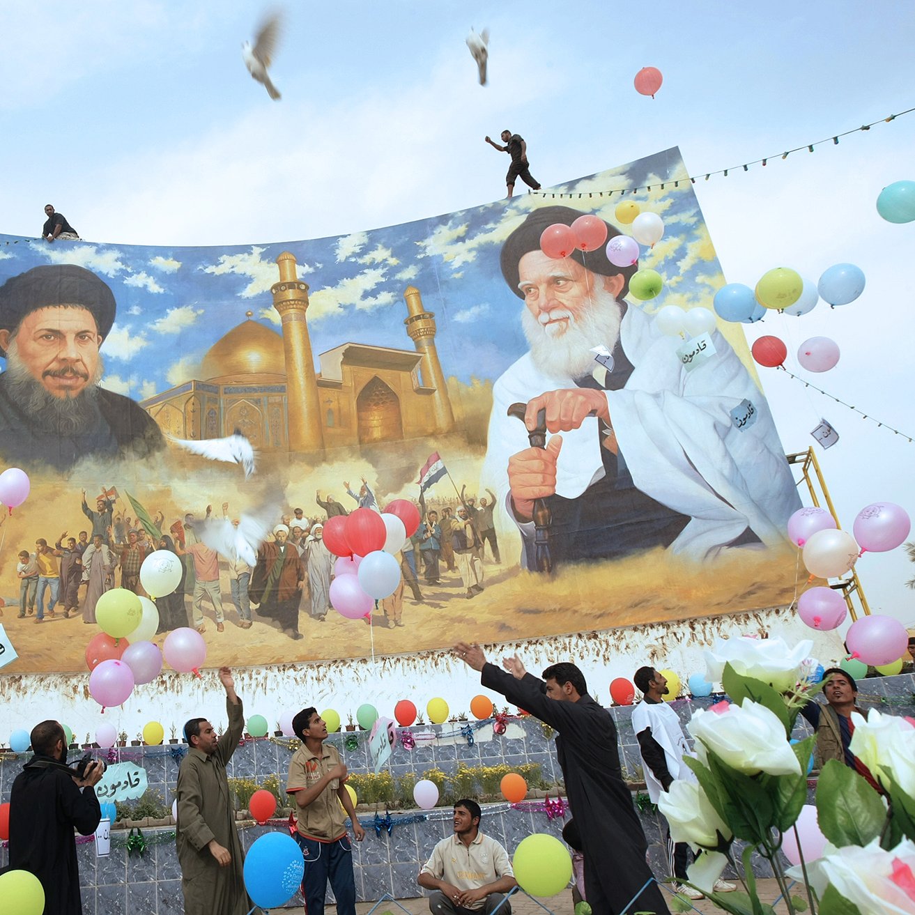 در این تصویر، تعدادی از مردم در حال برگزاری یک مراسم یا جشن هستند. در پس‌زمینه، یک دیوار بزرگ با تصویری از دو شخصیت سیاسی یا مذهبی به نمایش درآمده است. افراد در حال پرتاب بالن‌های رنگی و همچنین برخی گل‌ها به سمت هوا هستند. برخی از مردم در حال رقص و شادمانی دیده می‌شوند. پرنده‌هایی نیز در آسمان در حال پرواز هستند و فضای کلی تصویر روحیه مثبت و شادابی را به نمایش می‌گذارد.