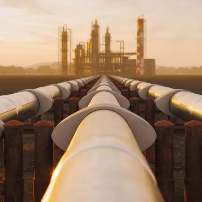 L'image montre une vue d'un long pipeline qui s'étend vers une installation industrielle en arrière-plan. Les tuyaux sont disposés sur des supports et semblent converger vers l'usine, éclairée par une lumière dorée, probablement au lever ou au coucher du soleil. L'environnement autour est vaste et dégagé, avec des montagnes lointaines à l'horizon, créant une ambiance industrielle mais aussi naturelle.