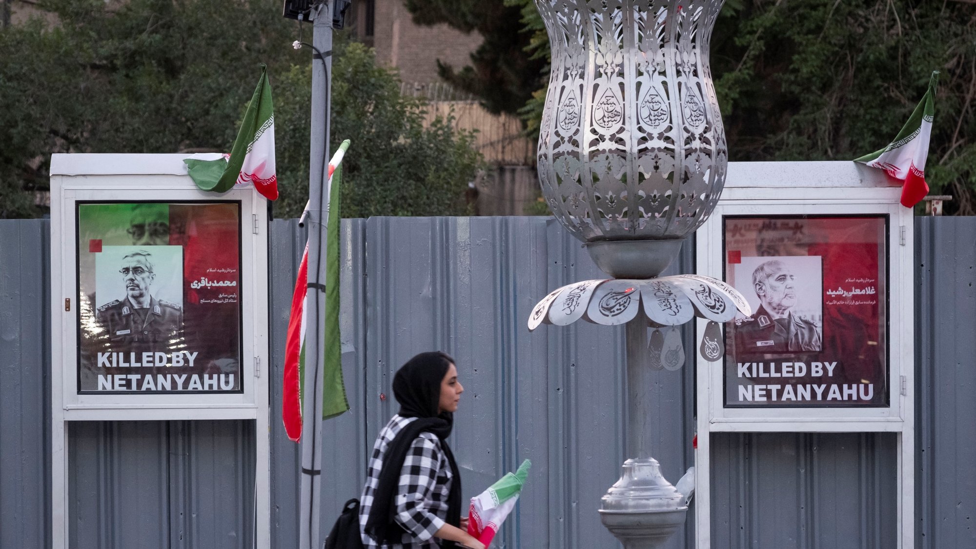A woman walks past two posters stating "Killed by Netanyahu," with flags nearby.