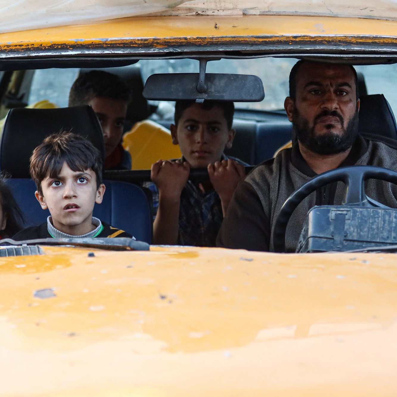 Un uomo alla guida di un'auto con bambini nel sedile anteriore, sguardi preoccupati.