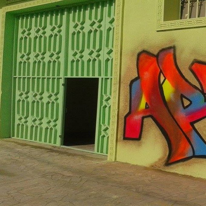 الصورة تظهر جدارًا ملونًا يحمل رسمة جرافيتي تحتوي على كلمة "ART" بألوان زاهية مثل الأحمر والأصفر والأزرق. الجدار هو بجانب باب أخضر فاتح، مما يضيف لمسة مميزة ومبهجة إلى المشهد. التصميم يعكس روح الفن والإبداع في البيئة المحيطة.