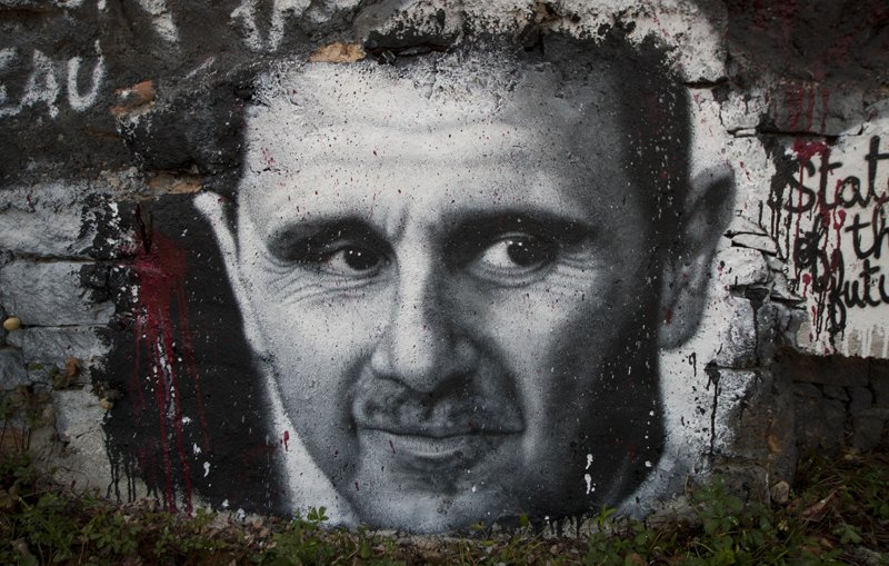 L'image montre un graffiti représentant un visage en noir et blanc sur un mur en pierre. Les traits du visage sont bien définis, avec un regard intense et expressif. Le fond est partiellement recouvert de peinture, et on peut voir des éclaboussures de couleur rouge, ajoutant une dimension dramatique à l'œuvre. Ce type d'art urbain est souvent utilisé pour faire passer des messages ou des commentaires sociaux.