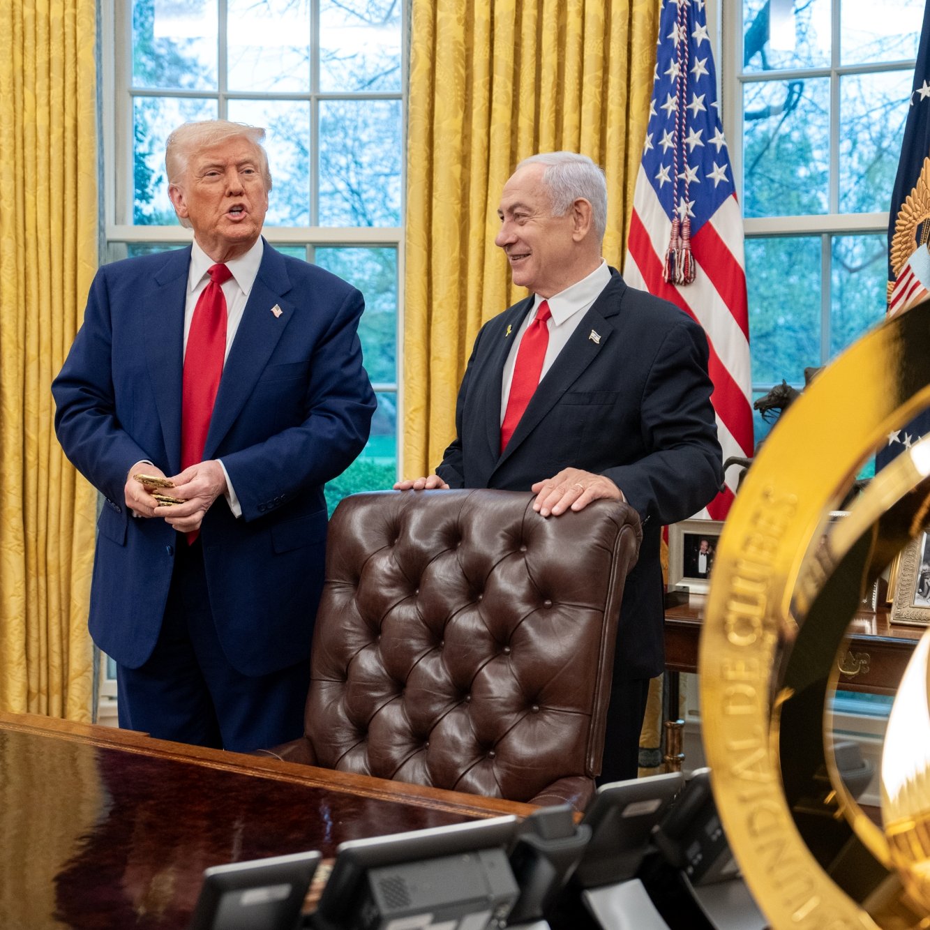 Due uomini in giacca parlano in una stanza elegante con tende gialle e bandiere.