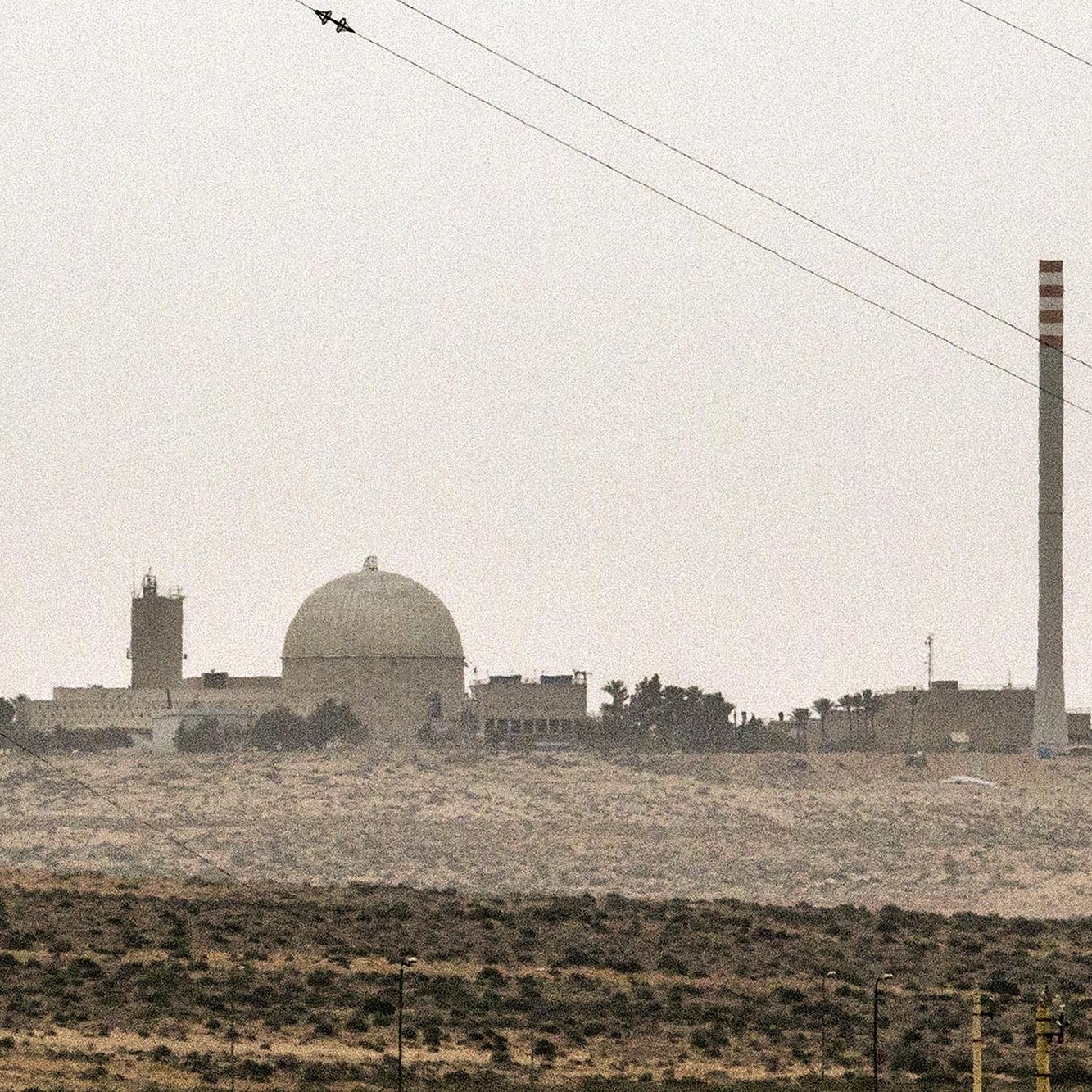 تصویر نمایی از یک تاسیسات صنعتی یا علمی را نشان می‌دهد که دارای یک گنبد بزرگ و چند ساختمان دیگر است. در سمت راست تصویر، یک دودکش بلند به چشم می‌خورد که ممکن است مربوط به فعالیت‌های صنعتی باشد. فضای اطراف تصویر سرسبز نیست و بیشتر به بیابان یا زمین‌های خشک مشابهت دارد. آسمان نیز ابری و کدر به نظر می‌رسد. این تصویر ممکن است به یک مرکز تحقیقاتی یا نیروگاه اشاره داشته باشد.