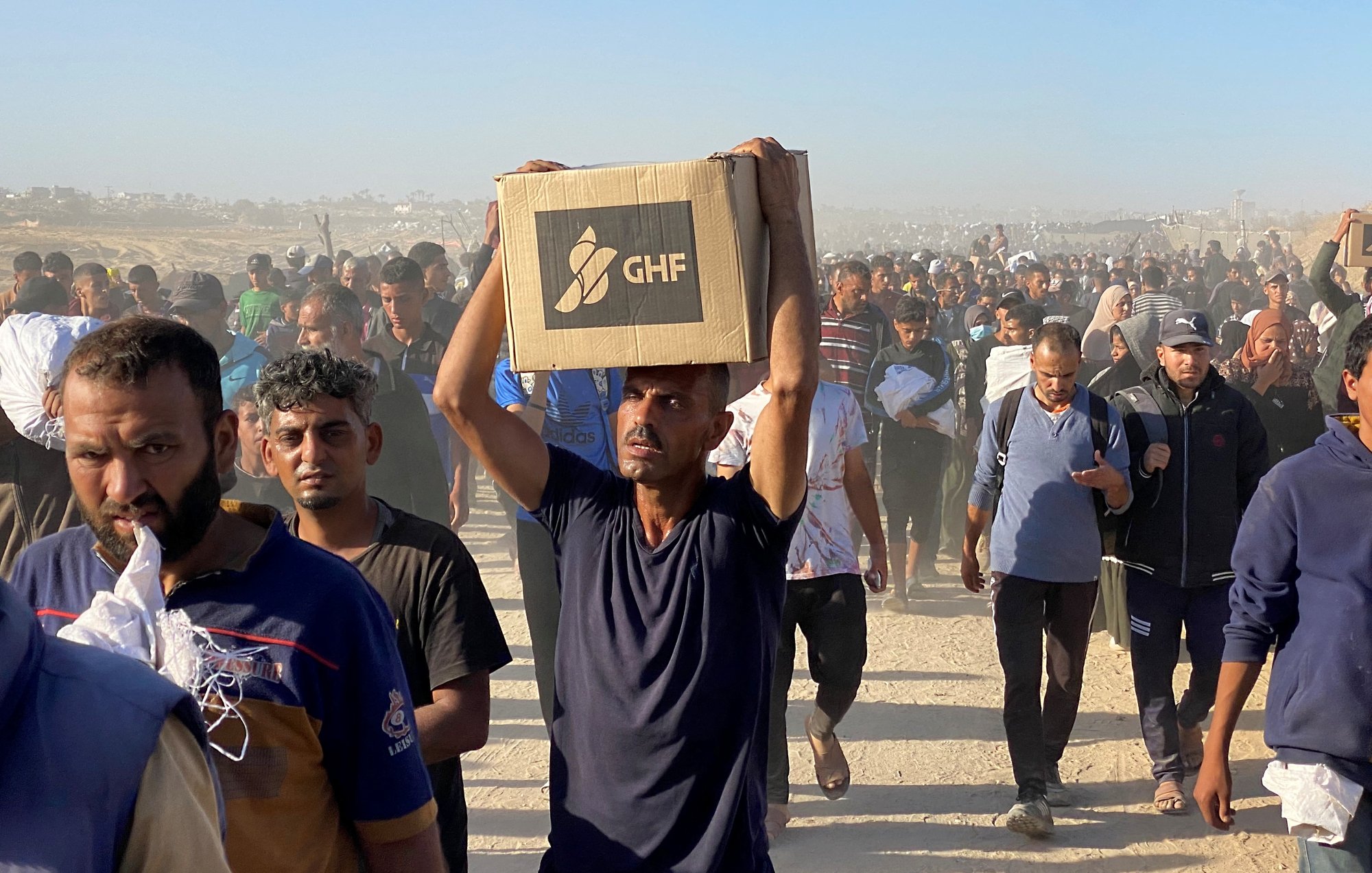 Un groupe de personnes marchent, portant des cartons dans un environnement poussiéreux.