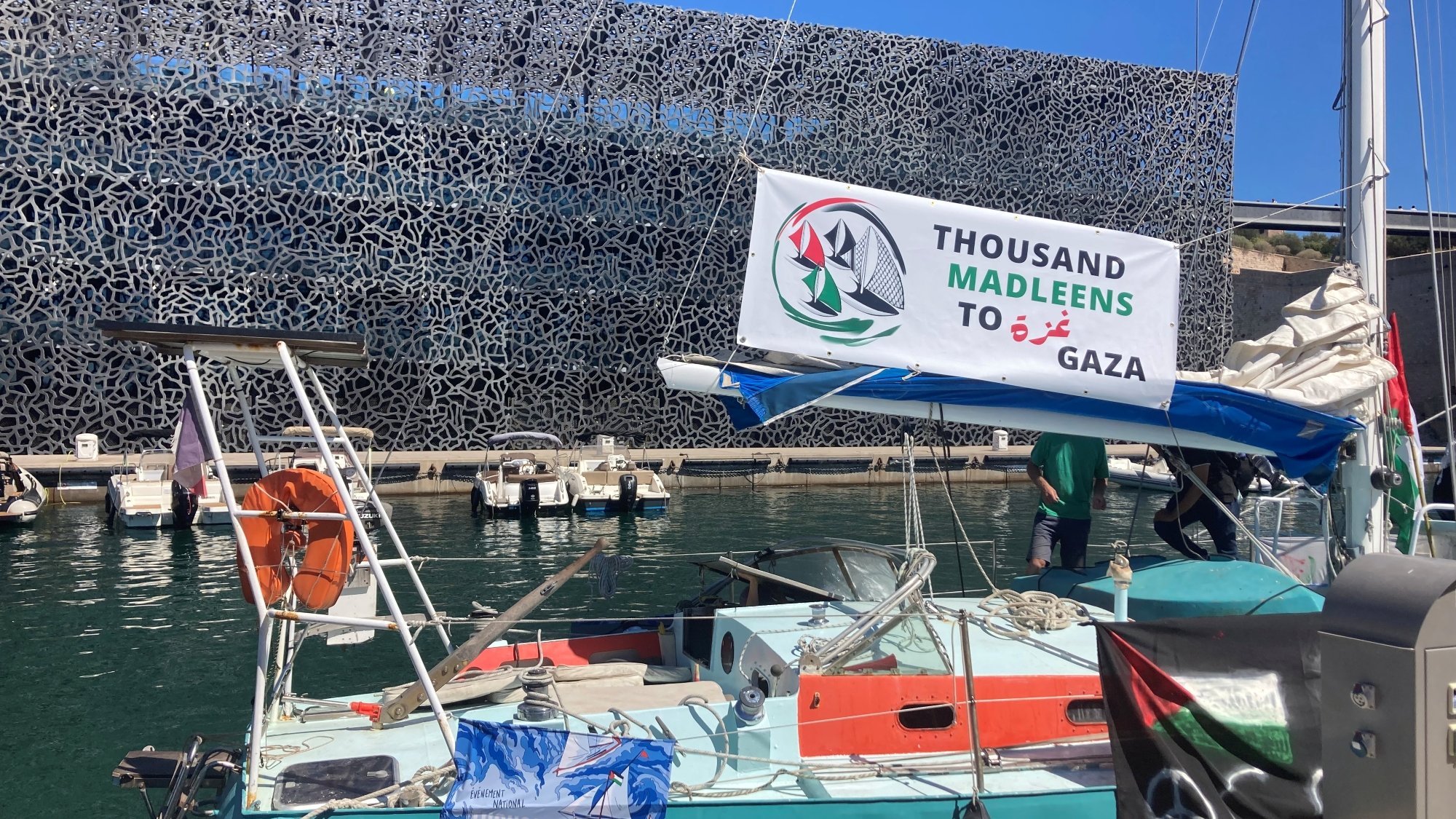 Una barca in un porto con un banner che supporta Gaza e un fondale moderno.