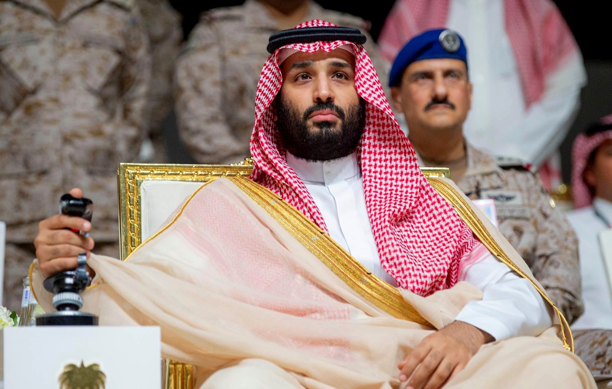 Un uomo in abiti tradizionali arabi, seduto su una sedia dorata, con uno sguardo serio.