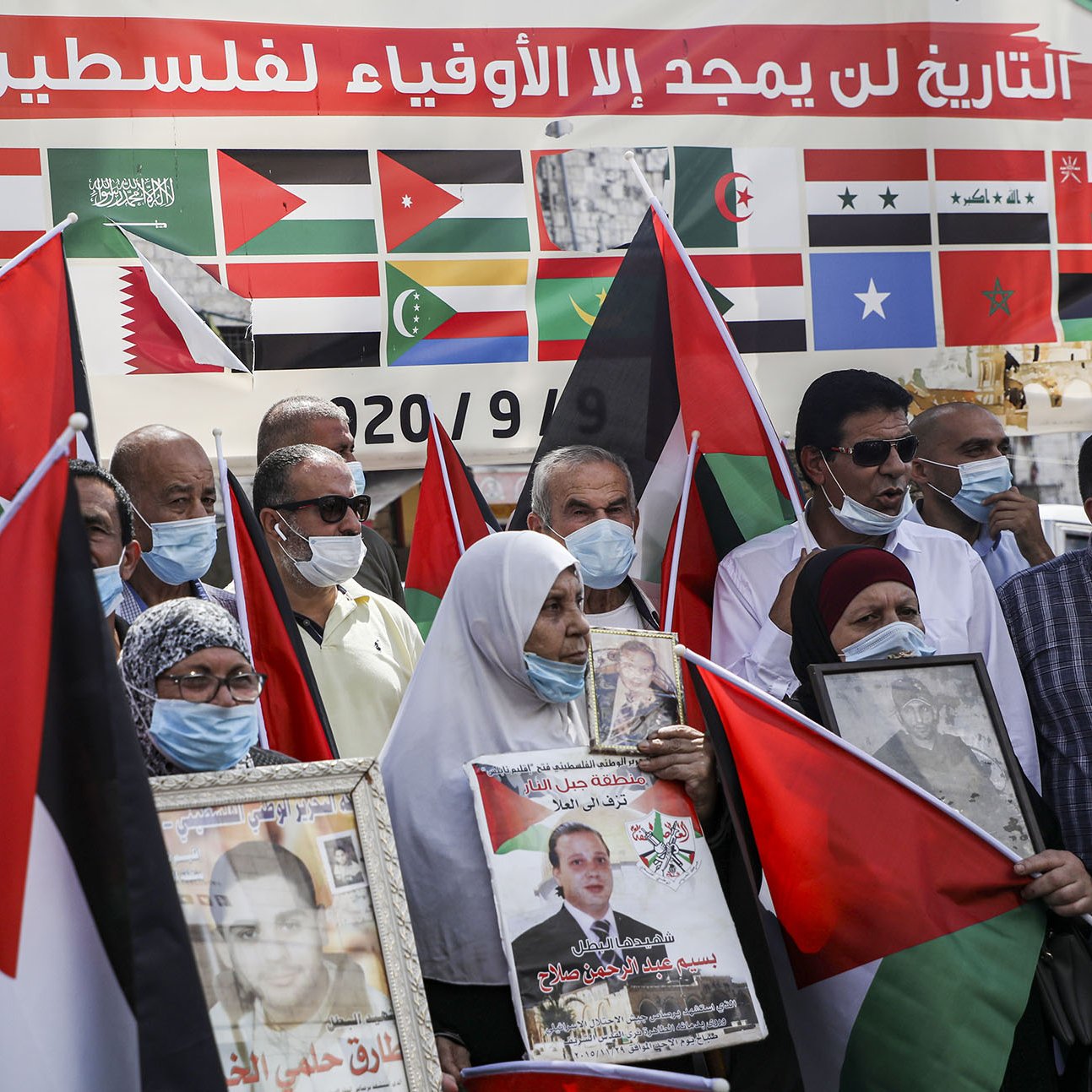 در این تصویر، گروهی از مردم در حال برگزاری یک تجمع هستند. آنها پرچم‌های فلسطین را در دست دارند و برخی از آن‌ها عکس‌هایی از شخصیت‌های مهم را حمل می‌کنند. بر روی پس‌زمینه، پرچم‌های کشورهای مختلف دیده می‌شود که نشان از حمایت‌های بین‌المللی از قضیه فلسطین دارد. همچنین، بسیاری از شرکت‌کنندگان دارای ماسک هستند، که ممکن است به دلیل رعایت مسائل بهداشتی باشد. احساس همبستگی و حمایت از آرمان فلسطین در چهره‌های آنها نمایان است.