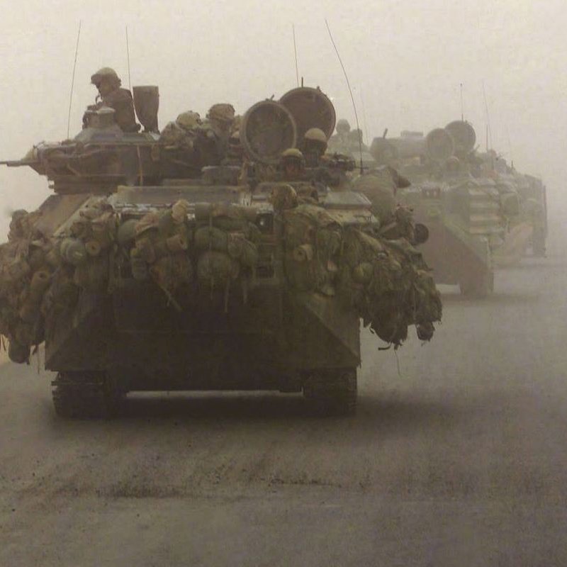 تظهر الصورة مجموعة من الدبابات تسير عبر ساحة مغطاة بالضباب أو الغبار. الدبابات محملة ببعض المعدات والعناصر العسكرية، ويبدو أن الجنود موجودون على متنها. الأجواء تبدو مشوشة بسبب الغبار، مما يعطي انطباعًا عن الظروف القاسية.