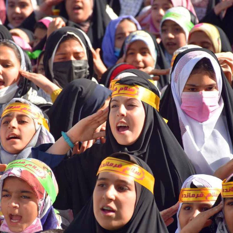 تظهر الصورة مجموعة من الفتيات يرتدين الحجاب، وهن يحتفلن أو يشاركن في فعالية جماعية. الفتيات متمركزات في مجموعة، ويبدين حماسًا ونشاطًا، حيث يرفعن أياديهن ويعبرن عن الفرح أو الحماسة. بعضهن يرتدين عصبات على الرأس مكتوب عليها كلمات تبدو تعبيرية. الجو العام في الصورة يوحي بالاحتفال والطاقة الإيجابية.