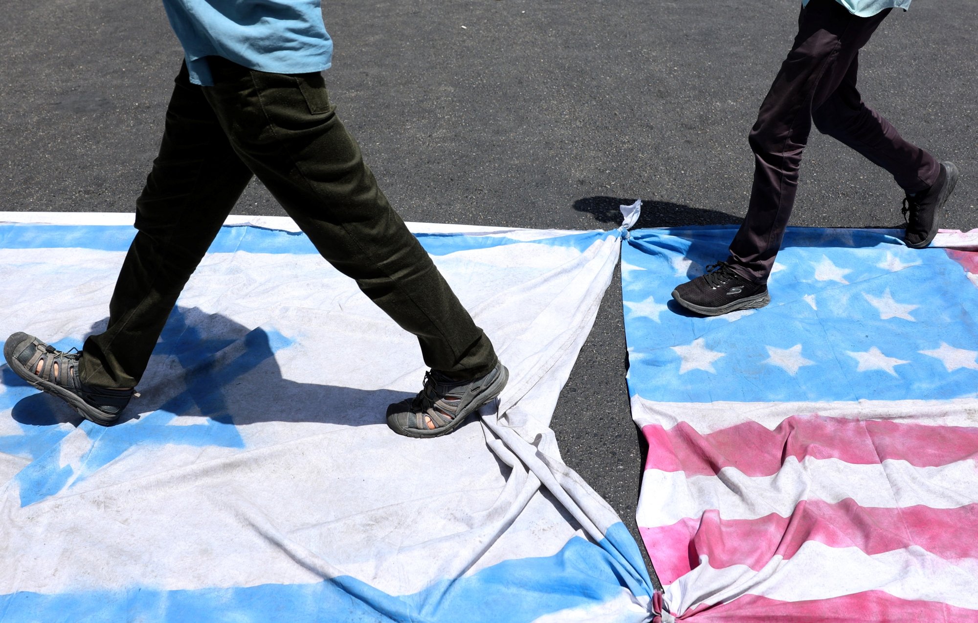 Deux personnes marchent sur des drapeaux américains et cubains étalés au sol.