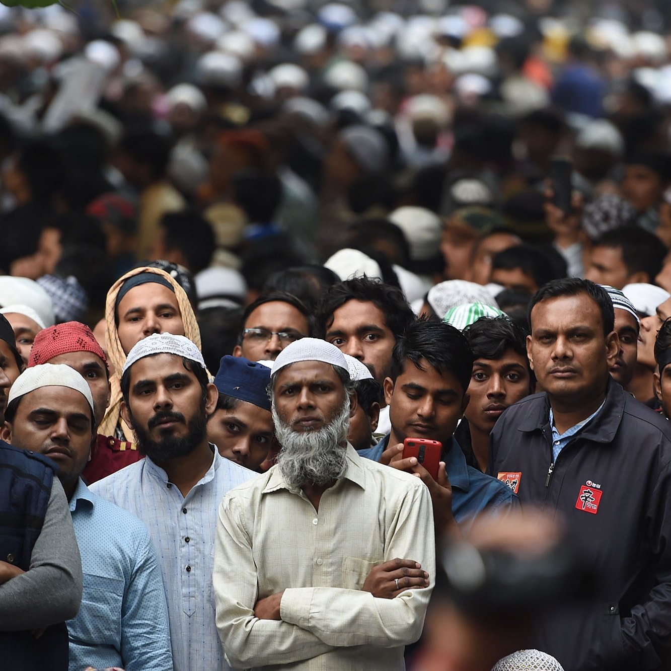 La imagen muestra una multitud de personas, muchas de las cuales llevan puestos kufis o tapones. La mayoría de las personas parecen estar prestando atención a algo en frente de ellos, algunos lucen serios y concentrados. Hay una gran diversidad de edades entre los asistentes y la atmósfera parece de expectativa. El fondo está lleno de más personas, lo que indica que es una reunión o evento masivo.