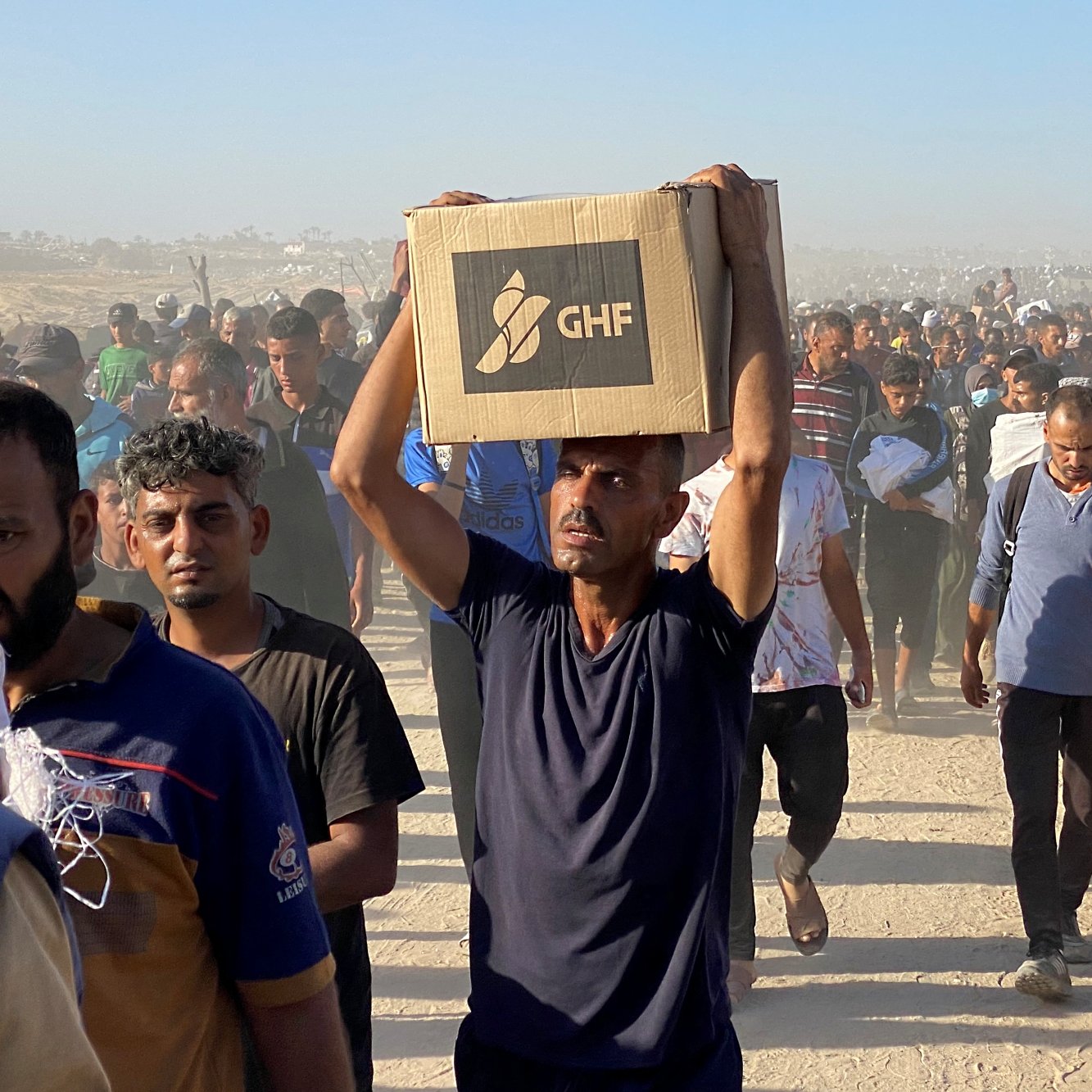 Un gruppo di persone cammina in un ambiente polveroso, portando scatole.