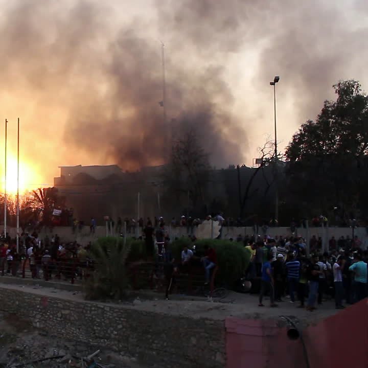 این تصویر نمایی از یک سناریو پرتنش را به تصویر می‌کشد، که شامل آتش و دود در آسمان است. غلظت دود نشان‌دهنده یک حادثه یا اعتراض شدید است. افرادی در پایین تصویر تجمع کرده‌اند و به نظر می‌رسد که در حال تماشا یا شرکت در یک رویداد مهم هستند. در پس‌زمینه، ساختمان‌هایی دیده می‌شود که به همراه تیرک‌های پرچم و تجهیزات دیگر قابل توجه است. این صحنه به طور کلی حس ناامنی و هیجان را منتقل می‌کند.