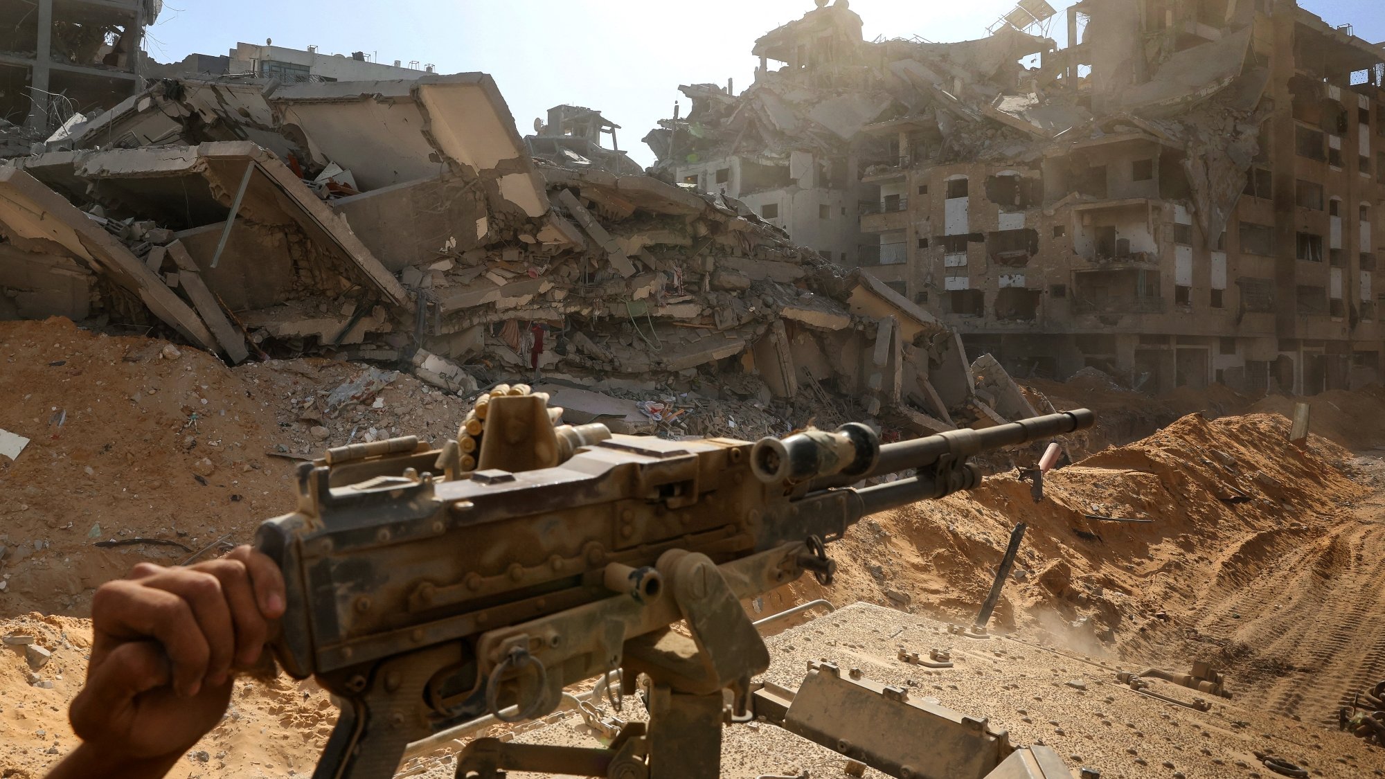 Un fusil pointé vers des bâtiments en ruines, sous un ciel lumineux.