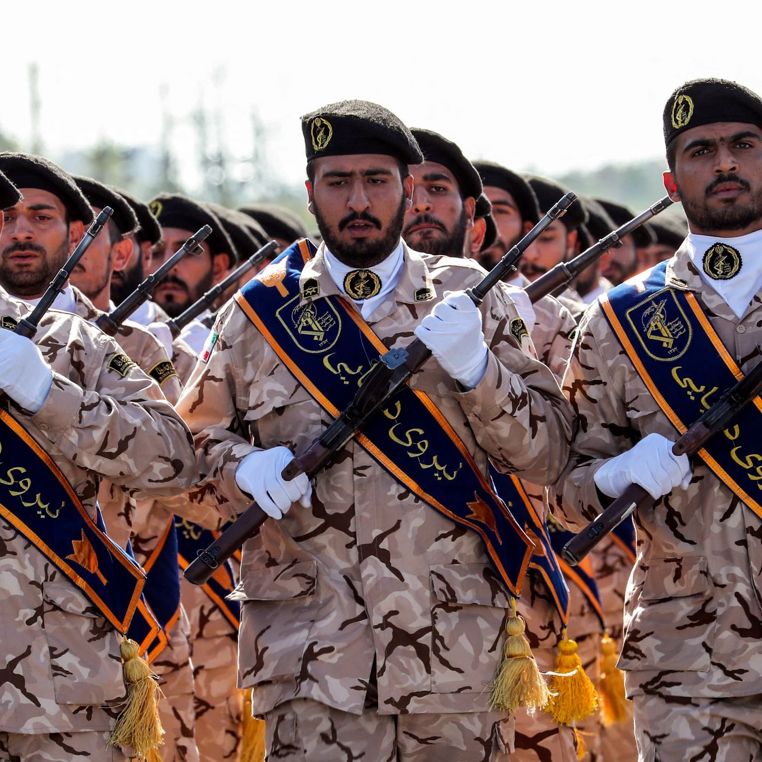 تظهر في الصورة مجموعة من الجنود يرتدون زيًا عسكريًا مموهًا، حيث يحمل كل منهم سلاحًا في يده. وهم يقفون بشكل منظم، ويبدو أنهم يشاركون في حفل استعراض أو مناسبة عسكرية. الجنود يرتدون زينة توحي بأنهم ينتمون إلى قوات معينة، ويظهر في الصورة تعبيرات جادة وملتزمة.