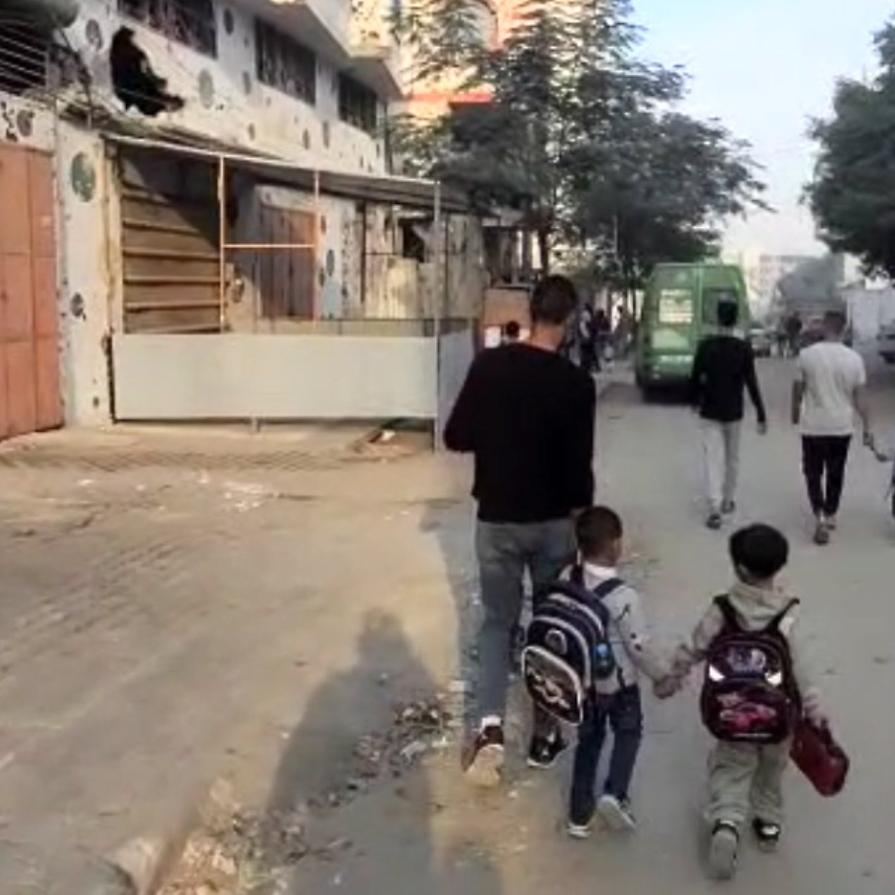 مردی با دو کودک با کوله‌پشتی در خیابان راه می‌روند. دیگران نیز در پس‌زمینه همراهشان هستند.