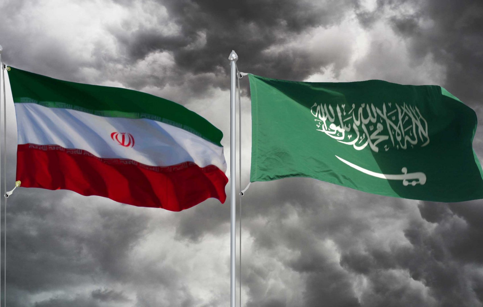 Nell'immagine sono visibili due bandiere: quella dell'Iran a sinistra e quella dell'Arabia Saudita a destra. Entrambe le bandiere sono sovrapposte a uno sfondo scuro e nuvoloso, creando un contrasto suggestivo. La bandiera iraniana è composta da bande orizzontali di verde, bianco e rosso, con lo stemma nazionale al centro. La bandiera saudita è verde, con la scritta in arabo e una spada bianca. L'insieme trasmette una sensazione di tensione e rivalità tra i due paesi.