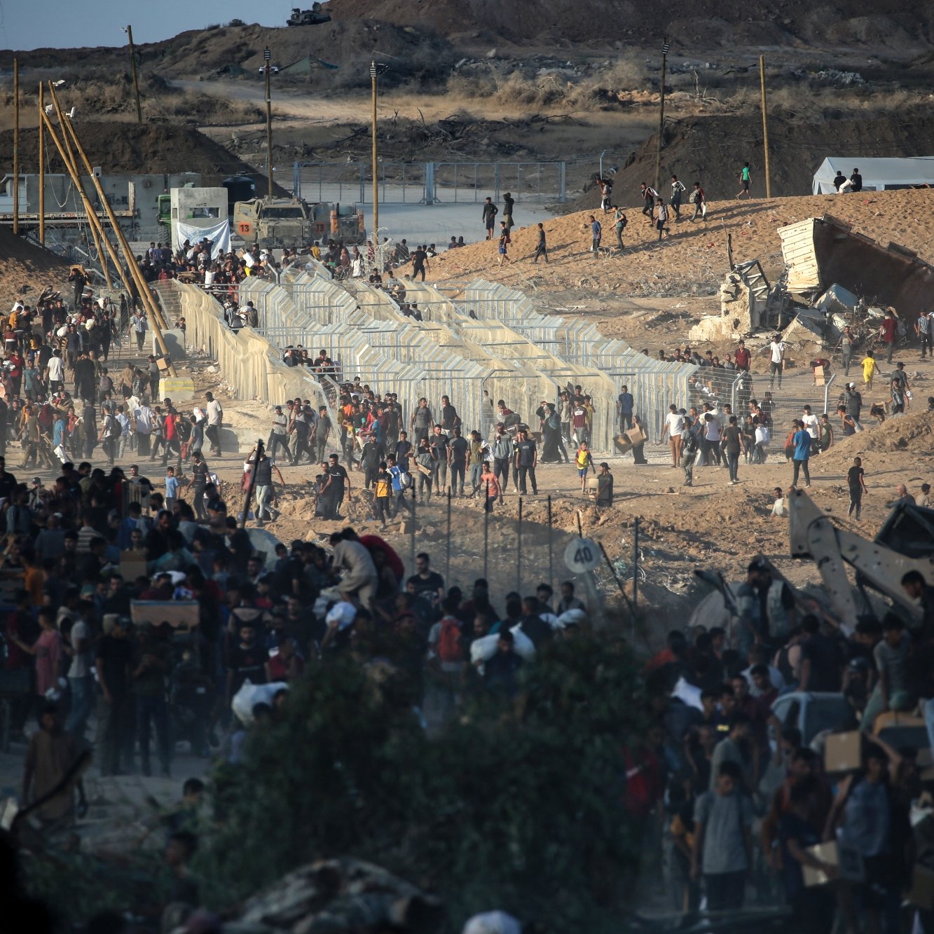 Persone in movimento vicino a barriere in un paesaggio arido e affollato.