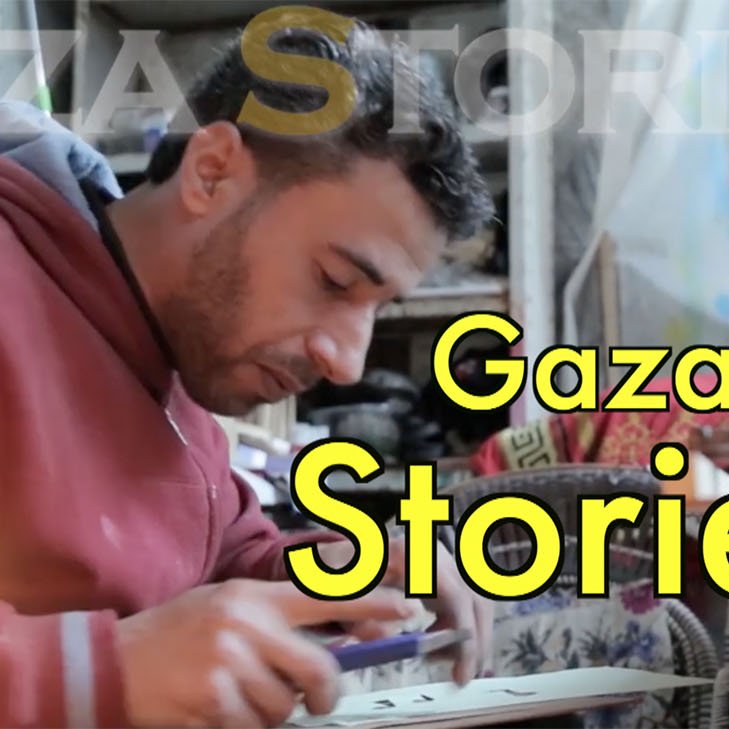 L'image montre un homme assis, probablement en train de travailler sur un projet créatif ou artisanal. Il porte un sweat à capuche rouge et semble concentré sur son activité. À côté de lui, une bougie est allumée, ce qui indique qu'il pourrait travailler dans un environnement peu éclairé. En arrière-plan, on aperçoit des éléments de décoration ou des fournitures, ce qui suggère une atmosphère artistique. En haut de l'image, on peut lire "Gaza Stories", ce qui laisse penser que le contexte est lié aux récits ou aux témoignages de Gaza.