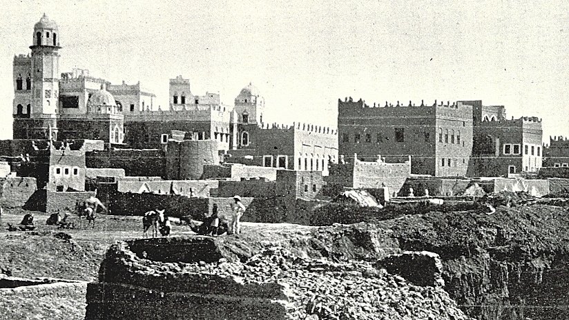 L'image présente un paysage urbain ancien, probablement d'une ville historique. On peut voir des bâtiments en pierre avec des détails architecturaux variés, tels que des tours et des terrasses. À l'avant-plan, on aperçoit des travailleurs, probablement engagés dans des activités agricoles ou de construction. La scène évoque une atmosphère à la fois rustique et animée, avec un ciel clair et des montagnes en arrière-plan qui ajoutent à la dimension historique et géographique de l'endroit. L'ensemble dégage une impression de temps révolu et de tradition.