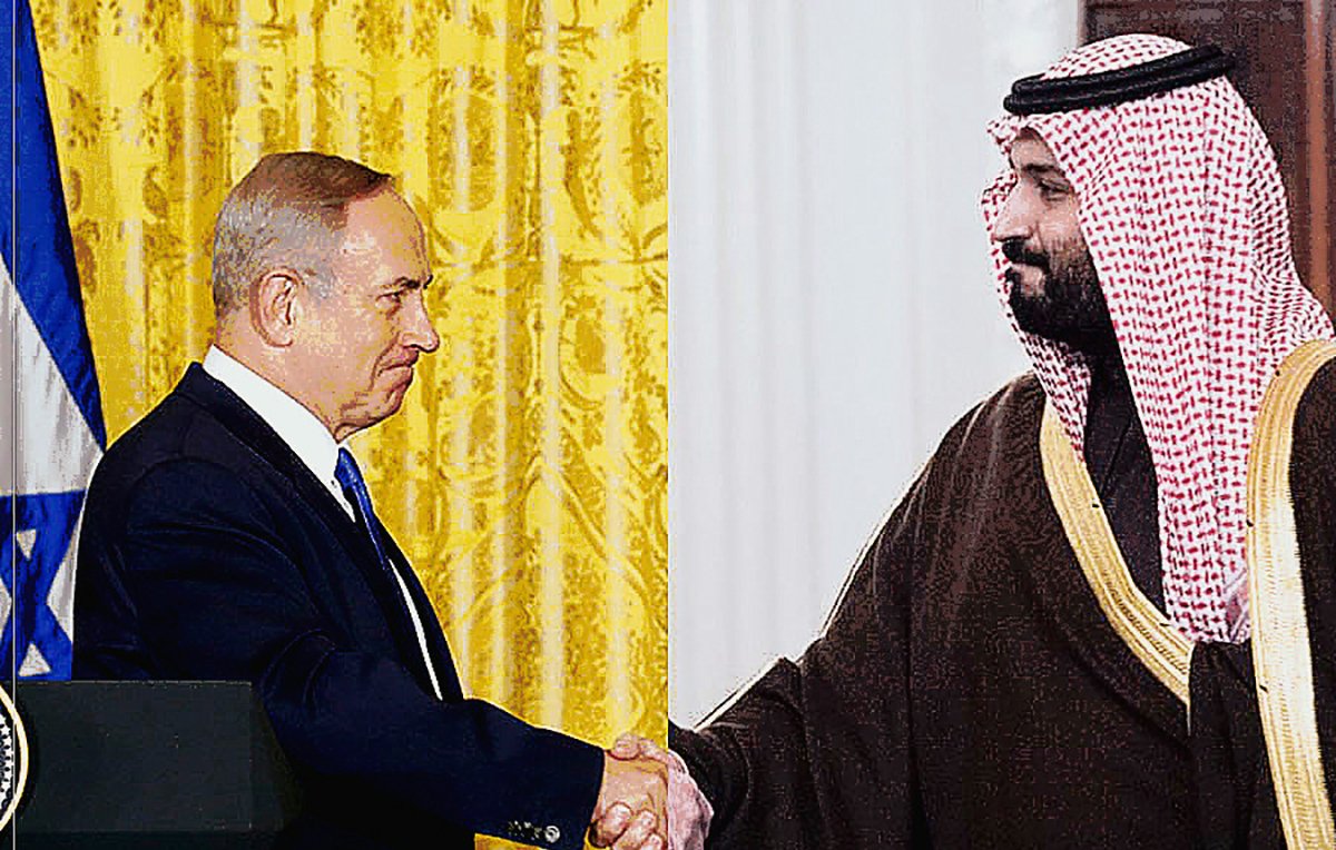 The image depicts two men shaking hands, symbolizing a diplomatic or cooperative gesture. On one side, a man is dressed in a dark suit, and on the other side, another man is wearing traditional attire, including a headdress. The background features a decorative curtain and possibly elements indicative of a formal setting, suggesting the significance of their meeting, likely related to political or international relations.