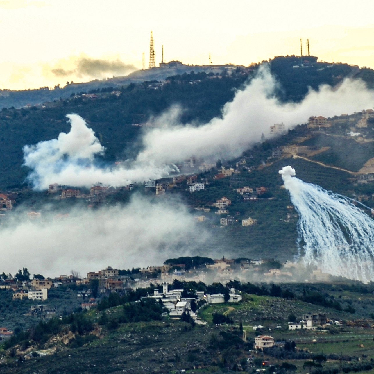 Una collina con case tra nebbia e spruzzi d'acqua, skyline industriale sullo sfondo.