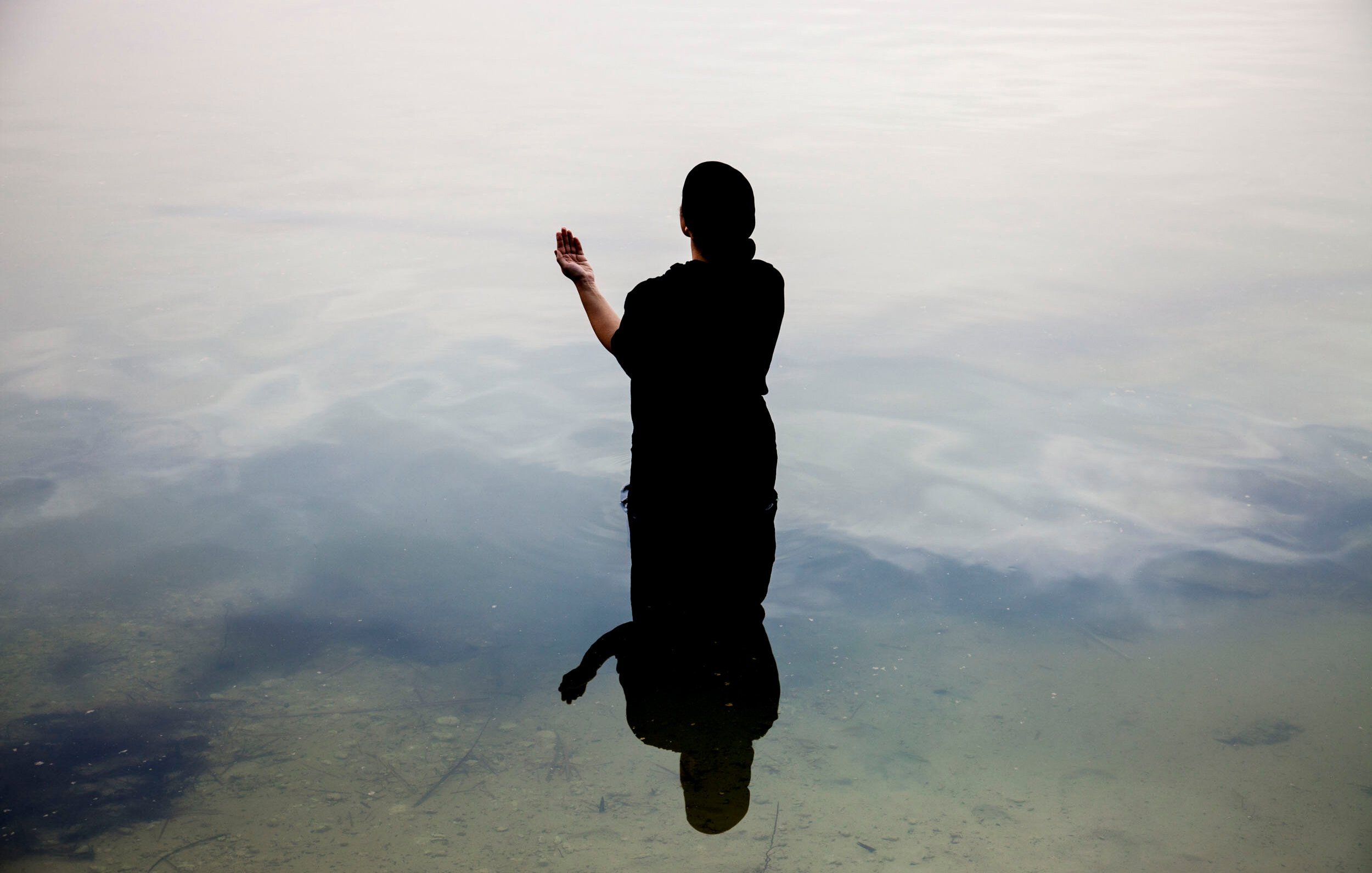 Une silhouette noire se tient dans l'eau calme, reflet visible à la surface.