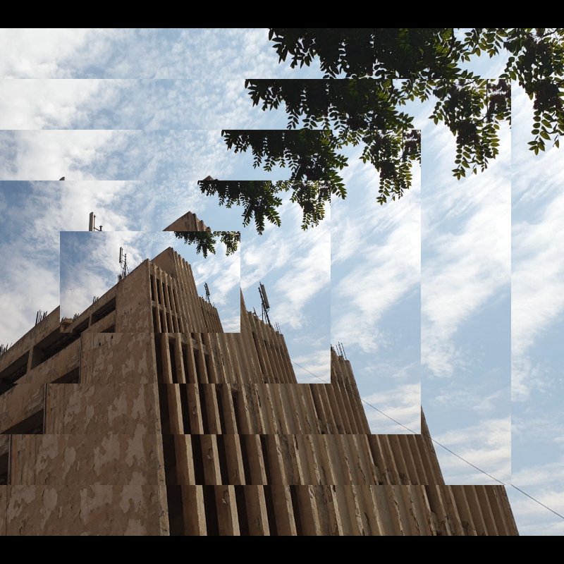 تظهر الصورة مشهداً لمبنى معاصر يظهر فيه تصميم معماري مميز، حيث يتكون المبنى من عدة طبقات وأشكال هندسية واضحة. السماء خلف المبنى محاطة بسحب بيضاء متناثرة، مما يضيف جمالاً إلى المشهد. في الزاوية العليا، هناك مجموعة من الأوراق الخضراء لشجرة تضفي لمسة طبيعية على الصورة. التصميم يبدو مزيجاً من الحداثة والطبيعة، مما يخلق تبايناً جميلاً بين العمارة والبيئة المحيطة.