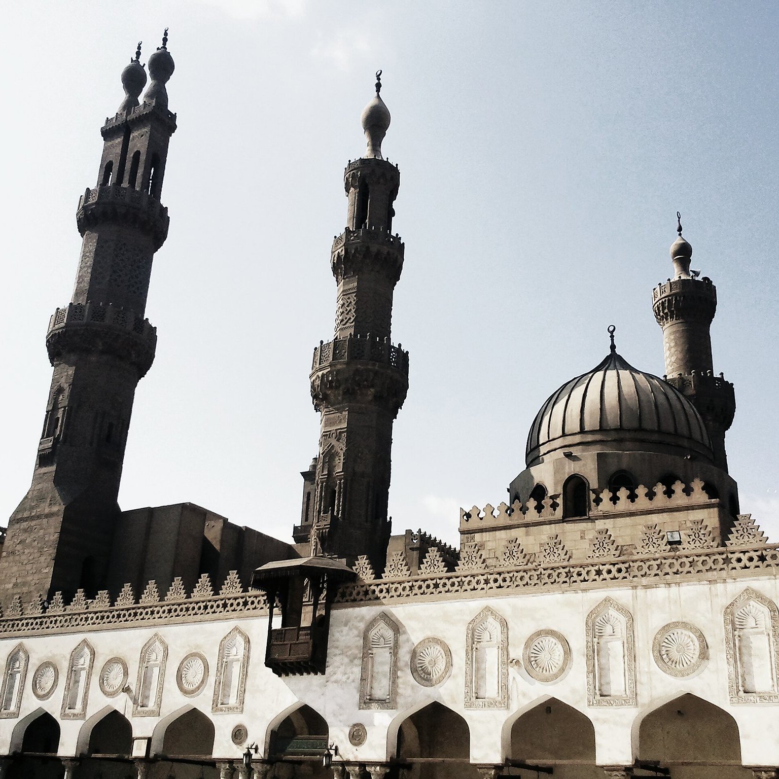 L'image montre une mosquée majestueuse avec deux minarets qui s'élèvent haut dans le ciel. La structure présente une belle architecture islamique, caractérisée par des arches décoratives et des motifs ornementaux sur les murs. Le dôme au centre ajoute à la grandeur du bâtiment, tandis que le ciel clair en arrière-plan donne une ambiance lumineuse à la scène. Les détails sculptés et la symétrie des éléments architecturaux témoignent d'un riche héritage culturel.