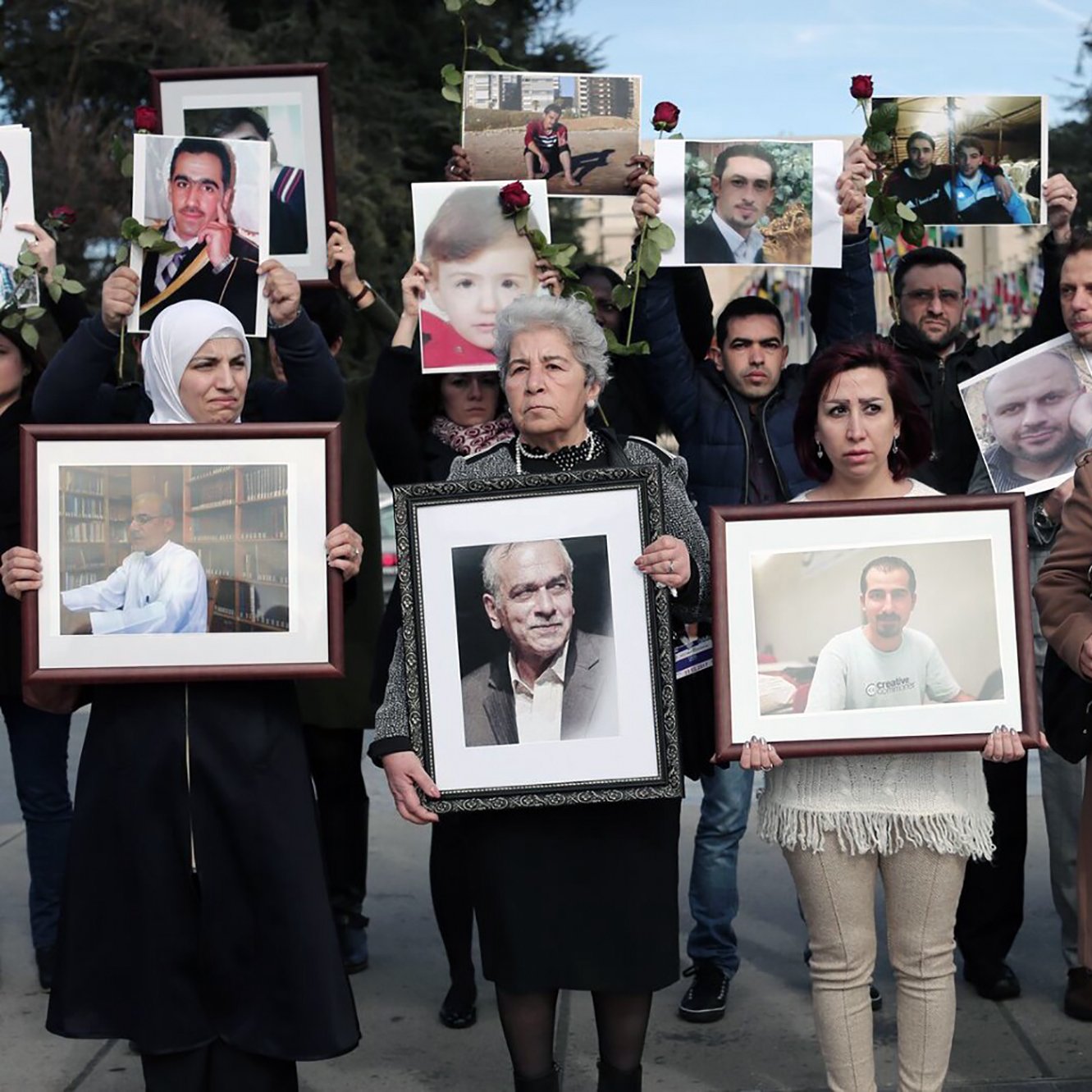 در این تصویر، گروهی از مردم در حال برگزاری تجمعی هستند. آن‌ها عکس‌هایی از افراد مختلف را در دست دارند که به نظر می‌رسد عزیزانشان باشند. در این تجمع، تعدادی زن و مرد حضور دارند، برخی از آن‌ها چهره‌هایشان را با گل‌هایی تزئین کرده‌اند. احساساتی نظیر ناراحتی و یادآوری در چهره‌های حاضرین مشهود است. این تصاویر ممکن است نشان‌دهنده یادمان یا اعتراضی برای یادآوری افرادی باشد که از دست رفته‌اند.