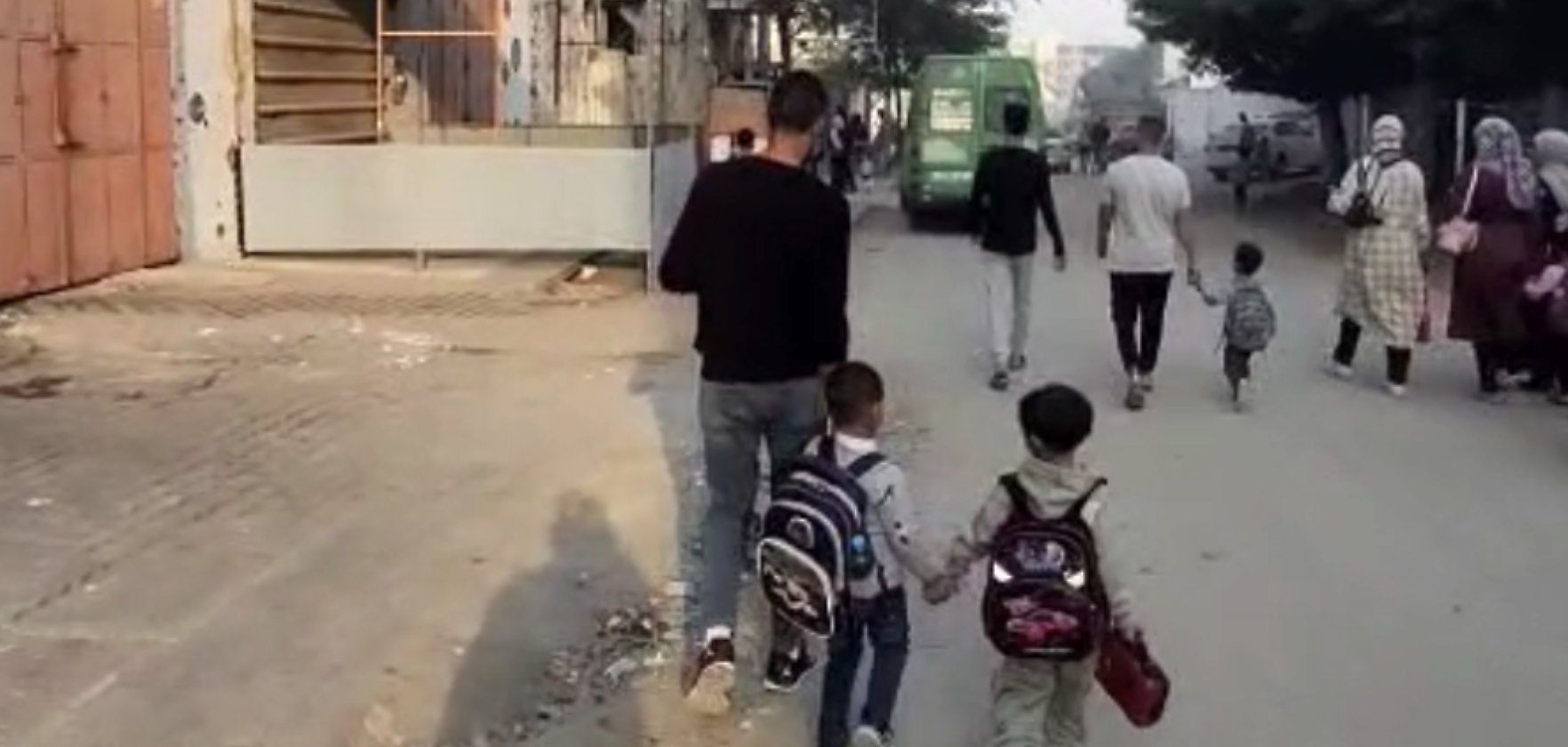 Des enfants marchent main dans la main avec un adulte sur une rue animée.