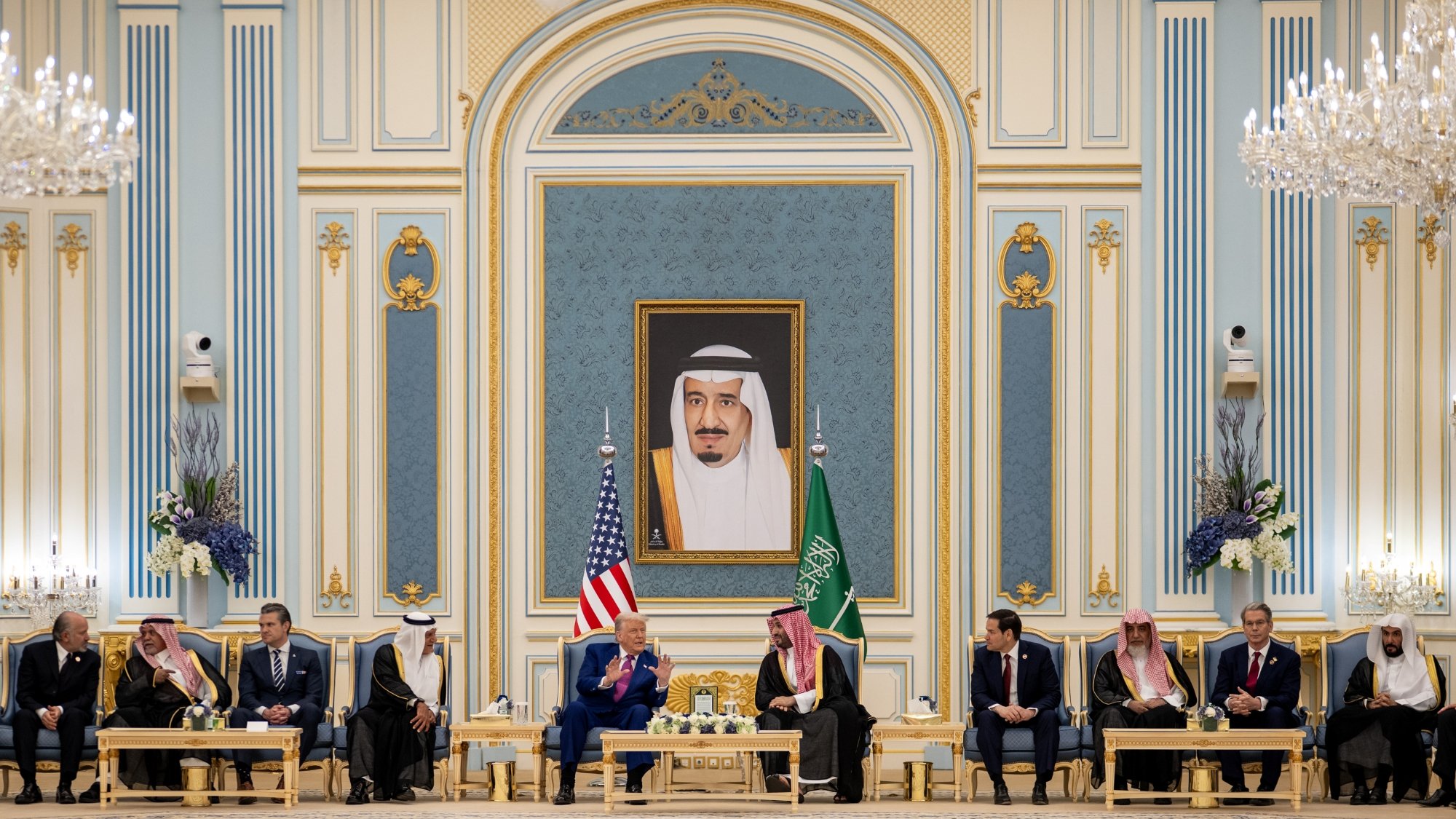 Réunion officielle dans un palais, drapeaux américain et saoudien, hommes en costume autour d'une table.