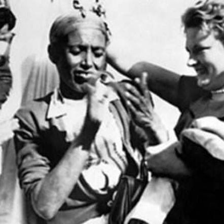 این تصویر یک صحنه اجتماعی و شاداب را نشان می‌دهد. در مرکز تصویر، یک زن و یک مرد در حال شادی و گفت‌وگو هستند. مرد ظاهراً لباس محلی یا سنتی پوشیده است و به نظر می‌رسد در حال رقصیدن یا آهنگ زدن است. زن دیگری که در کنار مرد ایستاده، لبخند می‌زند و به نظر می‌رسد از صحنه لذت می‌برد. همچنین چند نفر دیگر در زمینه تصویر دیده می‌شوند که به این شادی افزوده‌اند. فضای کلی تصویر به حس دوستی و جشن نزدیک است.