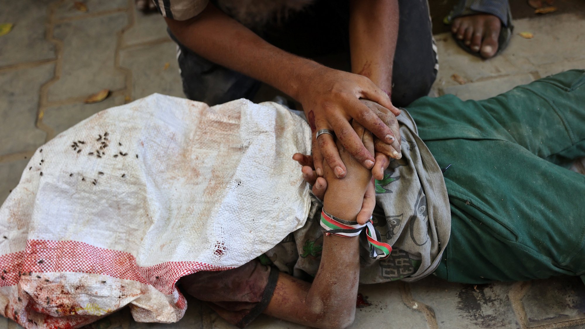 A person lying on the ground, covered in a cloth, with another person holding their hand.