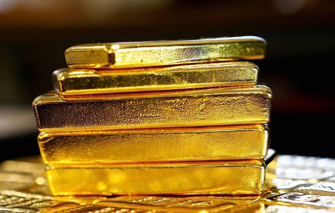 تظهر الصورة مجموعة من قضبان الذهب اللامعة، موضوعة بشكل متراص. القضبان ذات لون ذهبي براق، وتتميز بسطحها الأملس واللامع. يبدو أن القضبان ذات أحجام مختلفة، حيث تم ترتيبها بشكل عمودي، مما يبرز جمال الذهب وقيمته. يحيط بالصورة خلفية ضبابية وغير واضحة، ما يركز الانتباه على القضبان الذهبية.