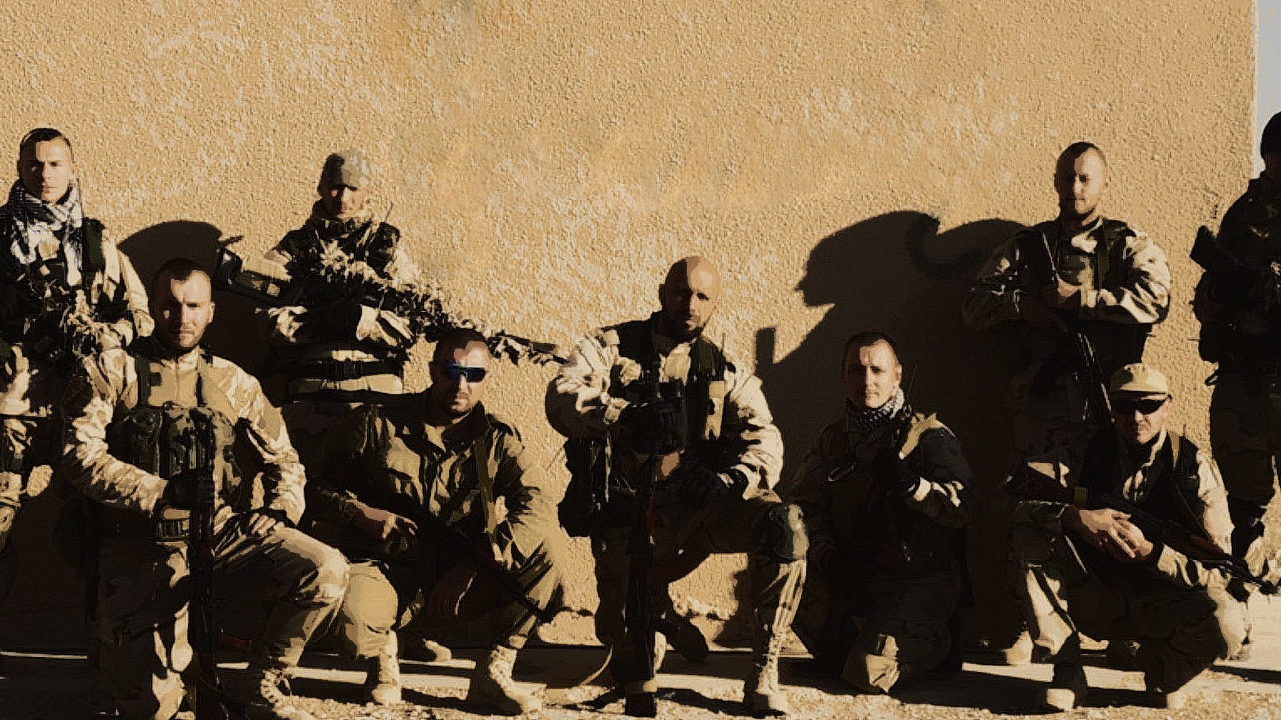 الصورة تظهر مجموعة من الجنود أو أفراد القوات المسلحة، يقفون معًا في وضعية تعكس القوة والانضباط. يرتدون زيًا عسكريًا ويحملون أسلحة، ويظهرون بمظهر جاد. الخلفية تبدو بسيطة، مما يركز الانتباه على المجموعة. تعكس الصورة روح الفريق والتضامن بين الأفراد.