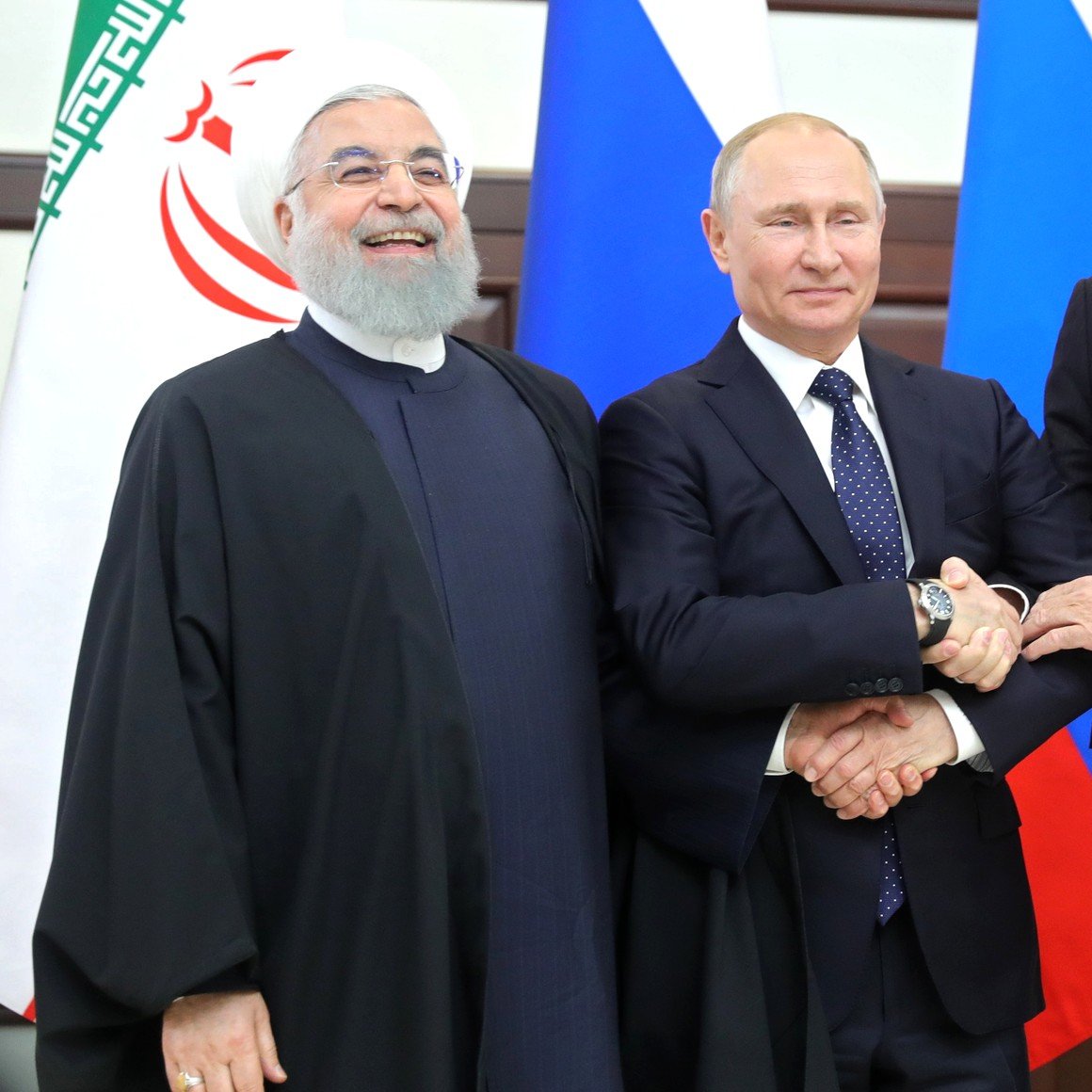 في الصورة، يظهر ثلاثة شخصيات سياسية بارزة. الشخص على اليسار يرتدي لباساً تقليدياً إسلامياً وله لحية. في الوسط، يظهر شخص يرتدي بدلة رسمية وهو يبدو كزعيم دولة. على اليمين، يظهر شخص آخر يرتدي بدلة أيضاً، وهو يبتسم. الثلاثة يقفون معاً ويبدو أنهم يتصافحون أو يضعون أذرعهم على بعضهم البعض. خلفهم توجد أعلام دول مختلفة، مما يشير إلى اجتماع رسمي أو قمة.