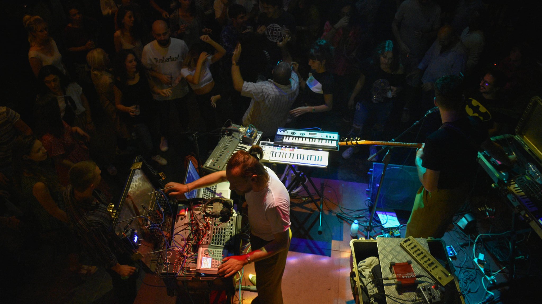 Concert animé avec des musiciens, des synthétiseurs et une foule dans une ambiance festive.