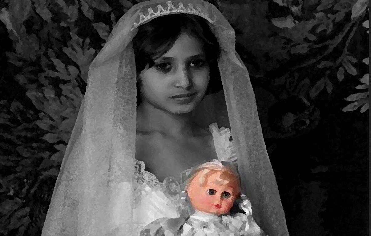 L'image montre une jeune fille portant une robe blanche et un voile. Elle tient une poupée dans ses bras. Le fond est sombre et texturé, ce qui met en valeur l'apparence délicate de l'enfant et de sa tenue. L'expression de son visage semble mélancolique et contemplative.