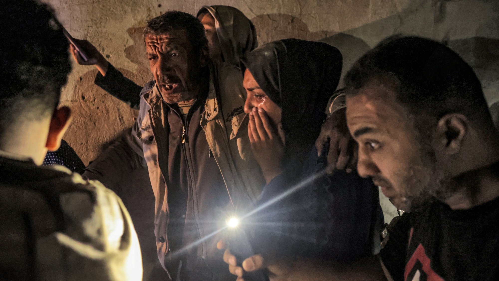 A group of people in a dim space, some worried, holding cell phone lights in tense expressions.