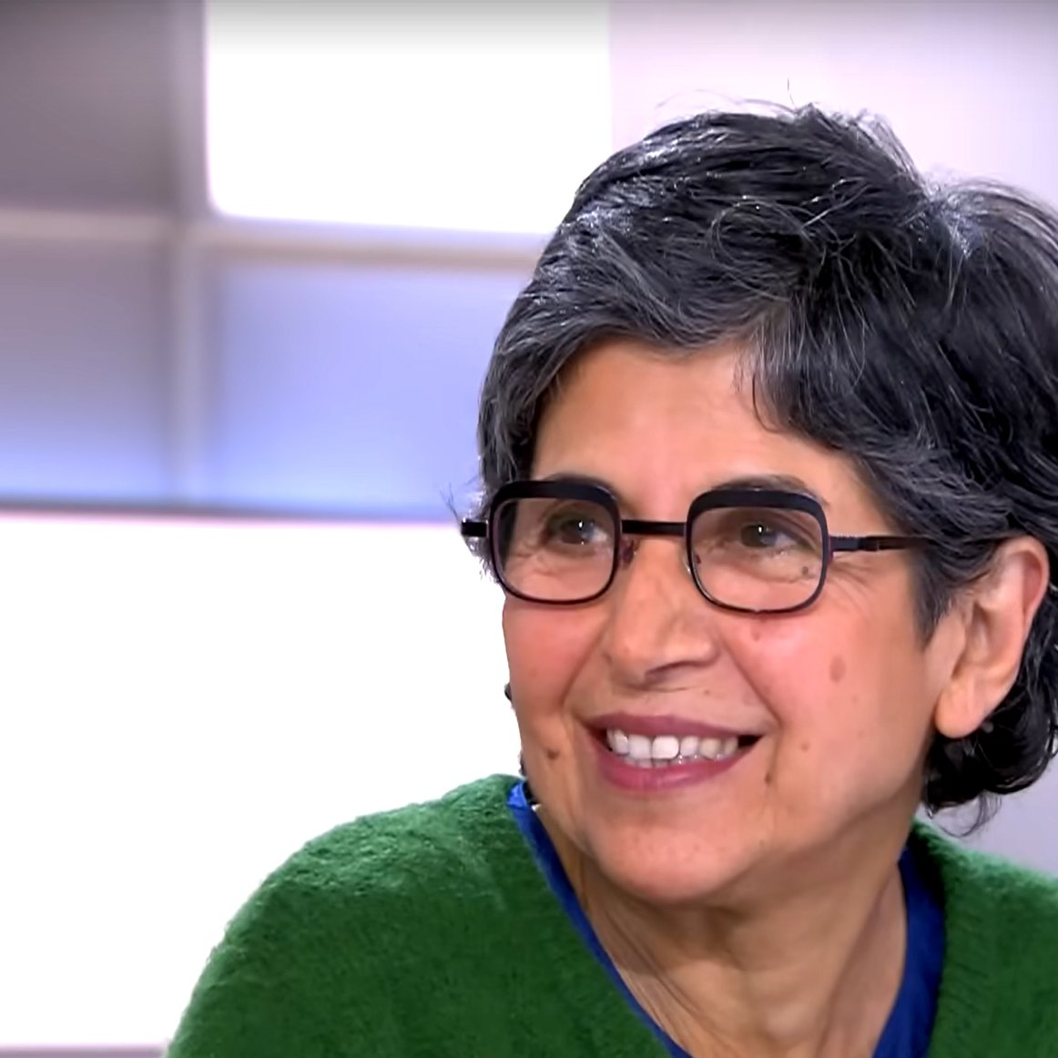 در این تصویر، فردی با موهای تیره و کوتاه و فر دیده می‌شود که عینکی به چشمانش زده است. او یک ژاکت سبز رنگ پوشیده و به سمت دوربین لبخند می‌زند. پس‌زمینه تصویر به صورت روشن و ساده است که توجه بیشتری را به چهره فرد جلب می‌کند. احساس او مثبت و دوستانه به نظر می‌رسد.